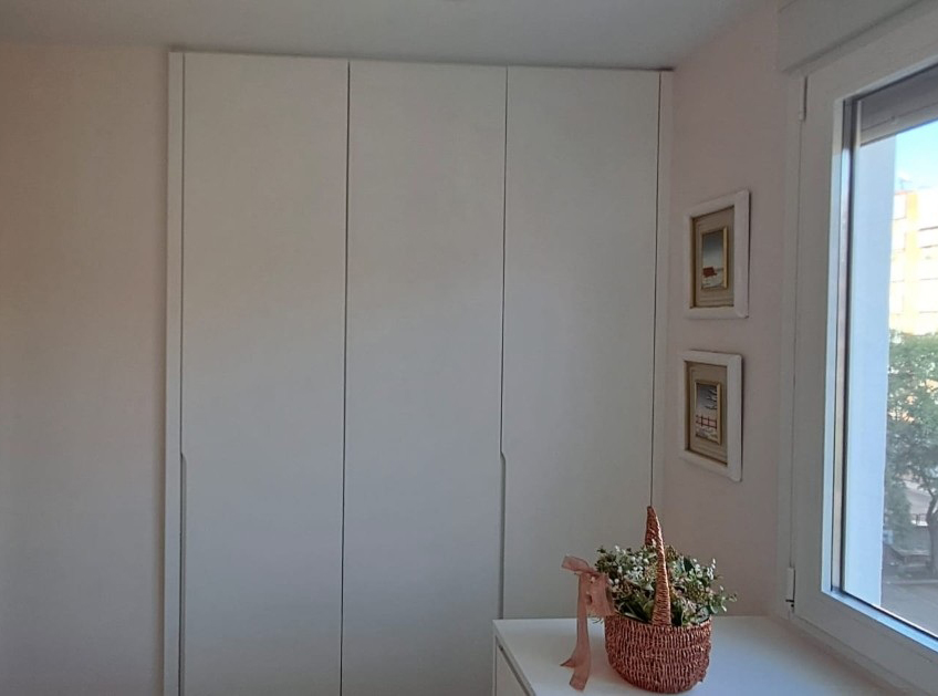 Armario empotrado blanco a medida junto a una ventana en dormitorio reformado
