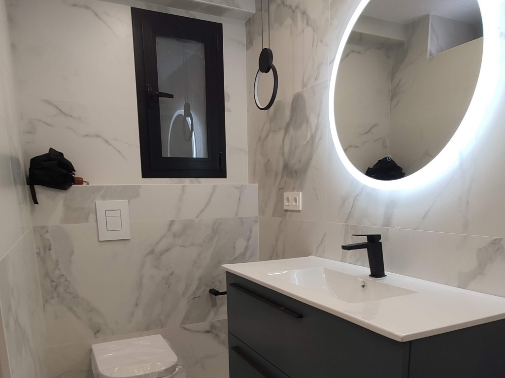 Baño reformado con mueble negro, lavabo blanco y espejo circular iluminado