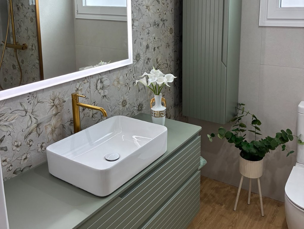 Baño reformado con mueble verde, lavabo sobre encimera y espejo retroiluminado