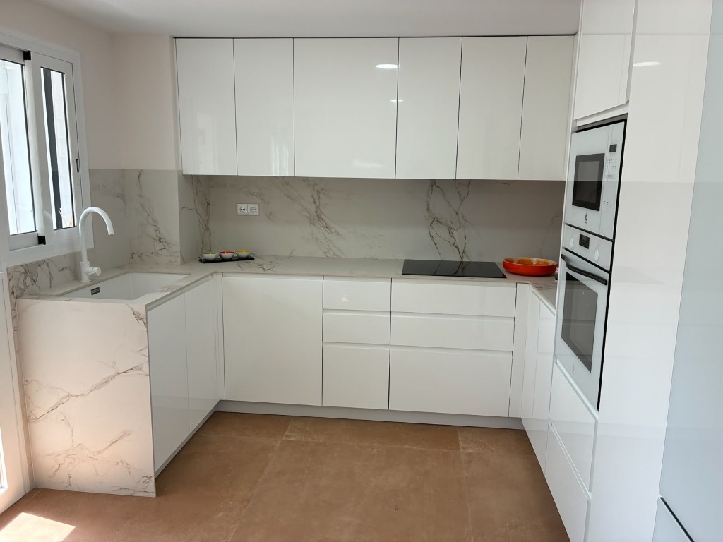 Cocina reformada con mobiliario blanco, encimera efecto mármol y electrodomésticos integrados