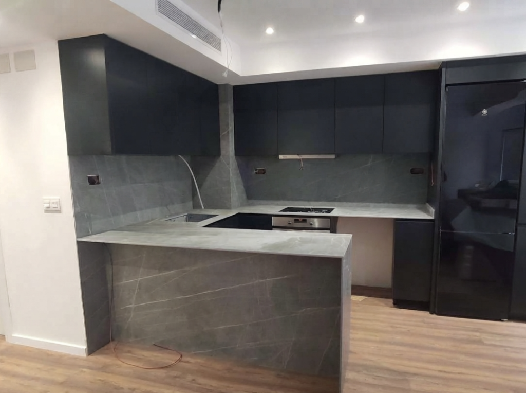 Cocina moderna con muebles negros, encimera y revestimiento efecto piedra gris