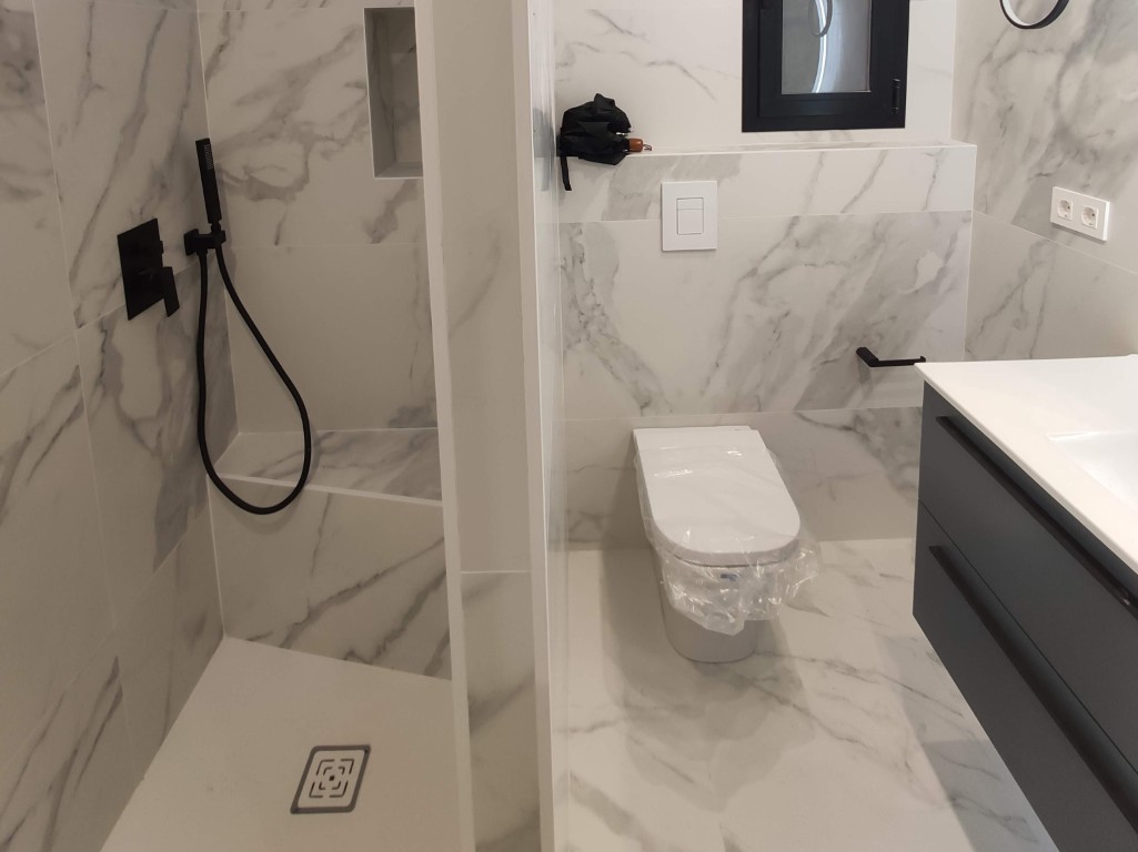 Baño reformado con ducha a ras de suelo y revestimiento efecto mármol