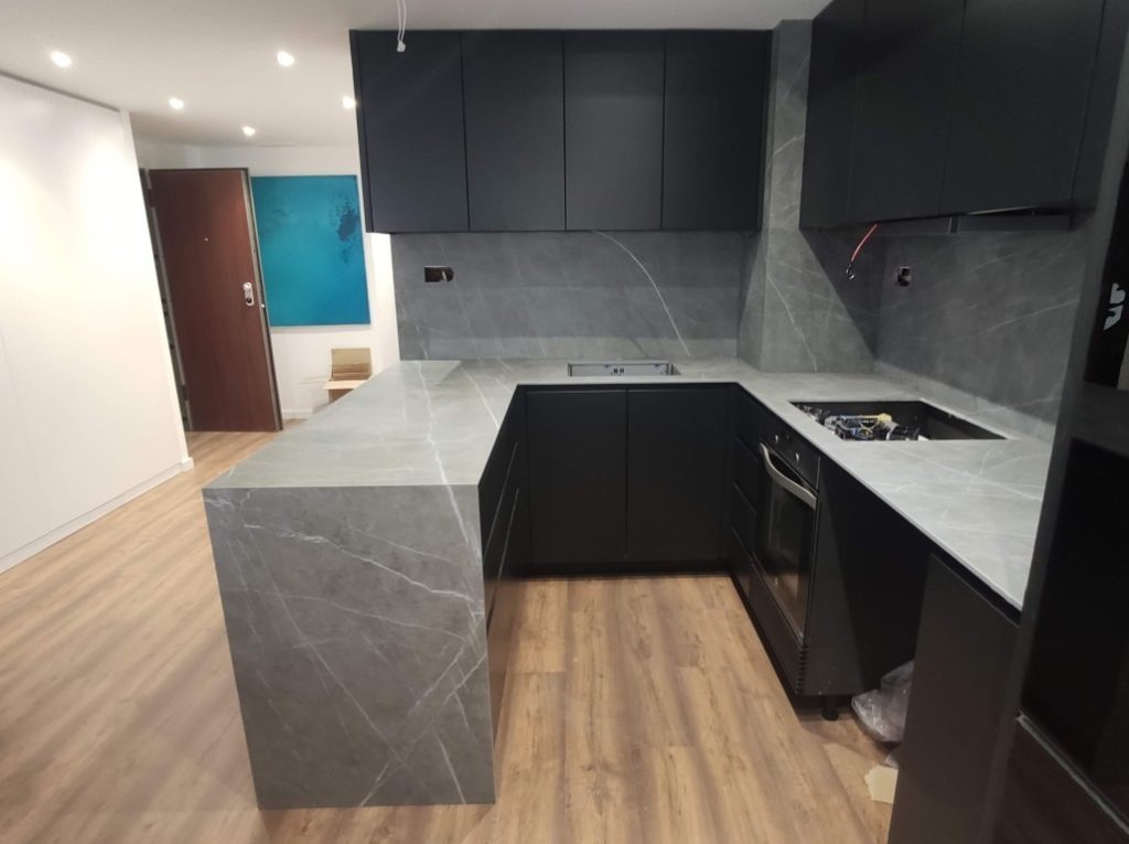 Cocina integral reformada con muebles negros, encimera gris y suelo de madera