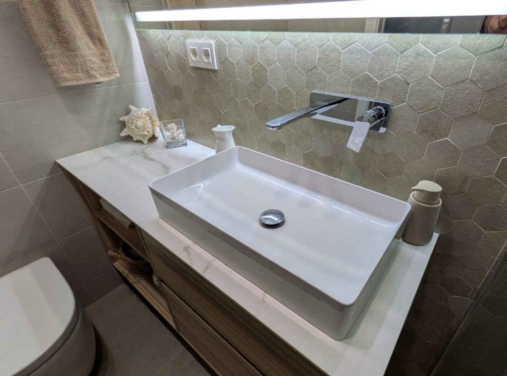 Lavabo sobre encimera con grifería mural en baño reformado de Valencia